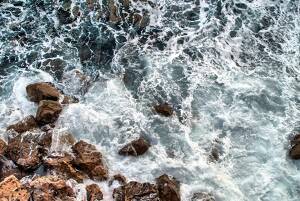 Luftaufnahme des Ozeans mit Wellen, die gegen Felsen schlagen.